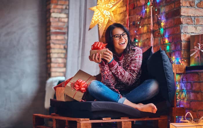 College brunette female dressed in a jeans and a red sweater posing on a sofa in a room with gifts