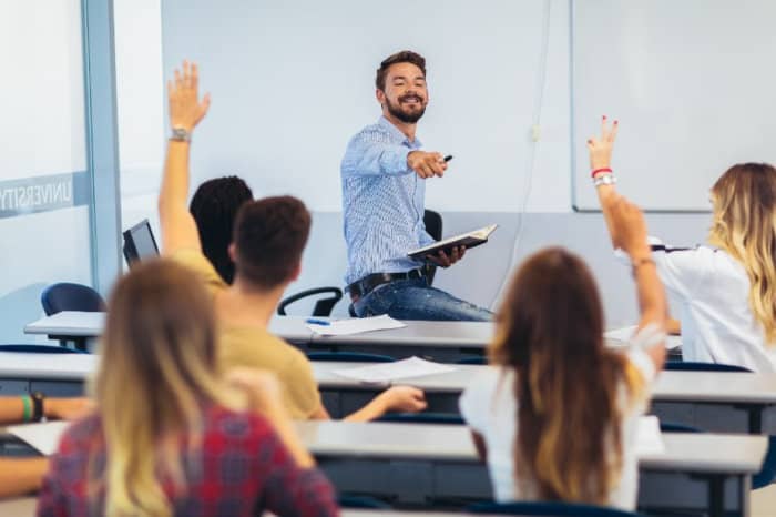 History teacher in class with kids raising hands to answer question