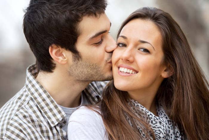 Close up portrait of boy kissing girlfriend on cheek outdoors.
