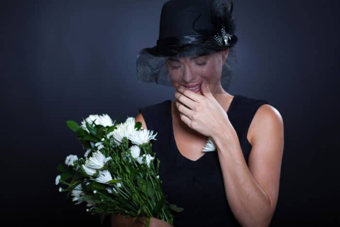sad widow with mourning clothing and flowers crying at husband's funeral