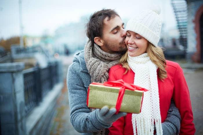mage of affectionate guy kissing his girlfriend while giving her present outside