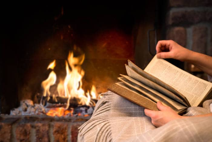 woman reading book by fireplace