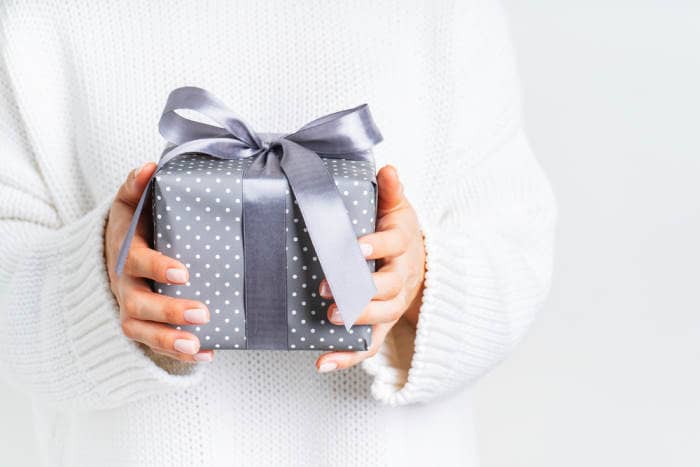 Female in woolen white sweater holding a gift box with a bow. Anniversary gift for friend.