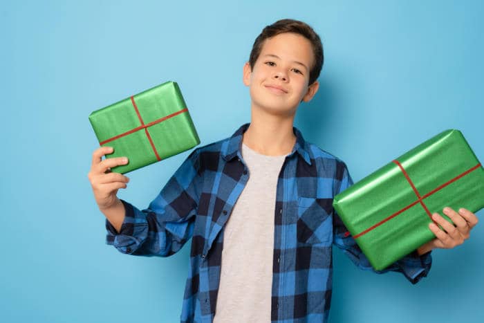 Happy teen boy holding many present and gift boxes isolated over blue background.